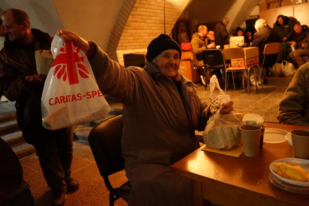 En eldre ukrainsk kvinne smiler mens hun viser frem en pose med mat hun har fått fra hjelpeorganisasjonen Caritas